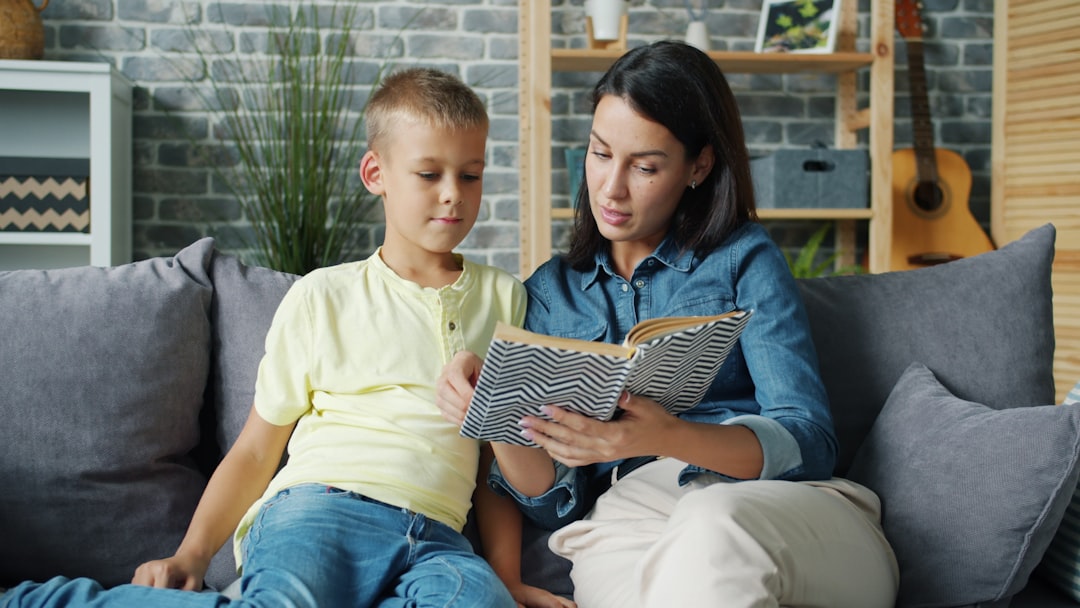 Caring mom is reading book to little child cute boy sitting on sofa in living room and enjoying interesting story. Childhood and parenthood concept.