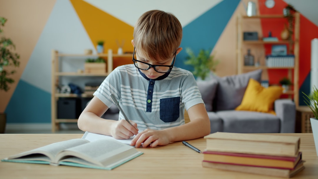 Portrait of cheerful child boy doing homework then looking at camera and smiling sitting at desk at home. Education, childhood and intellect concept.
