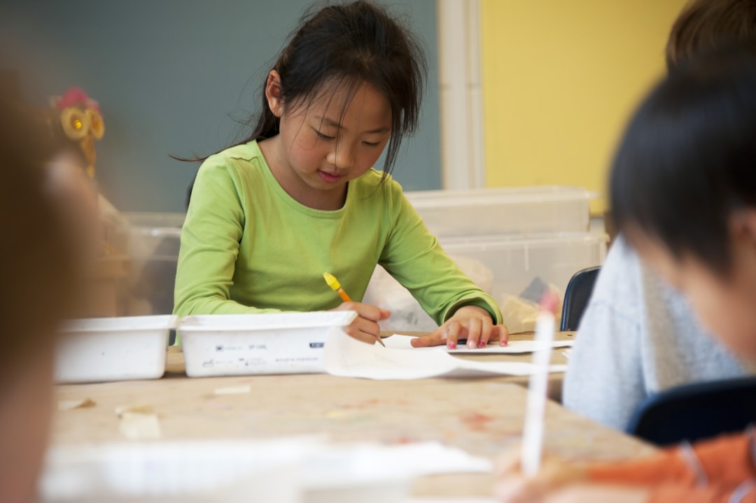 Captured in a metropolitan Atlanta, Georgia primary school, this photograph depicts a young Asian-American schoolgirl, who was in the process of drawing with a pencil on a piece of white paper atop a table that had been covered by a layer of removable brown paper. It is important to know that these objects are known as fomites, and can act as transmitters of illnesses. 