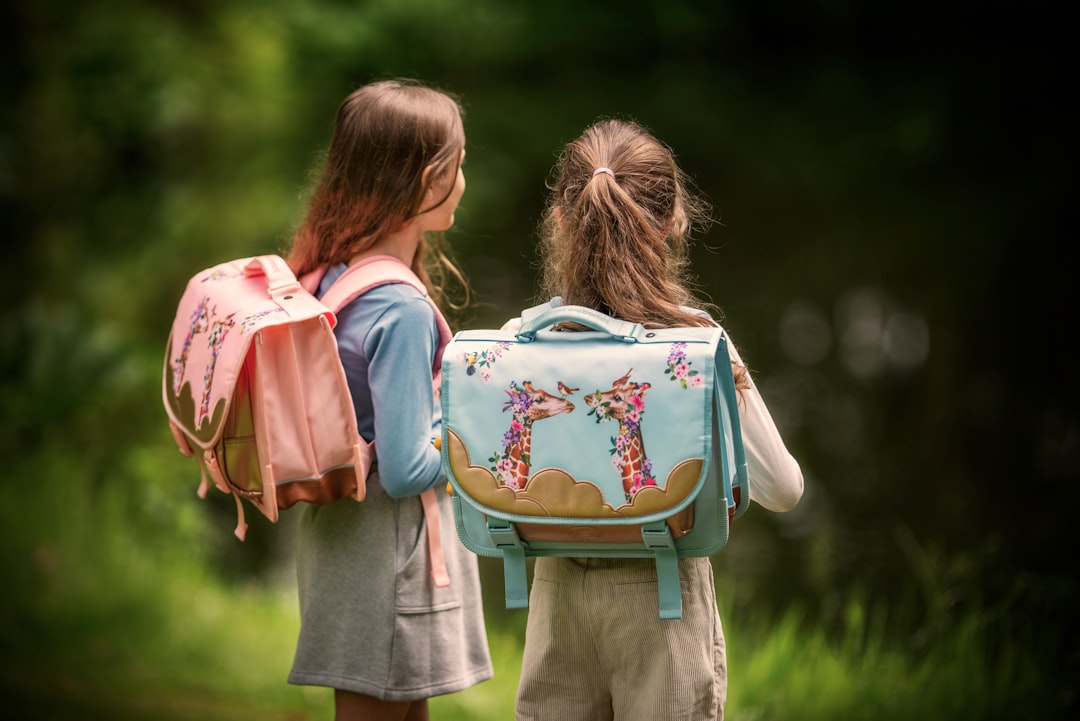 Two girls stand with their backpacks near water.